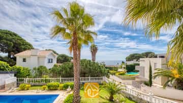 Vista exterior desde Villa Estrella que muestra una piscina en primer plano, palmeras, balaustradas blancas y villas vecinas bajo un cielo azul con nubes dispersas.