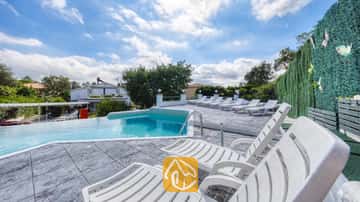Piscina privada con múltiples tumbonas de plástico blanco en una terraza enlosada en Villa Geolouk, España.