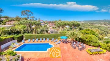 Piscina exterior privada en Villa Jaruco, que cuenta con un patio de terracota bordeado de tumbonas a rayas azules y blancas, y un juego de comedor bajo el cielo azul.