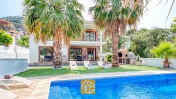Piscina privada con azulejos de mosaico azul y tumbonas sobre el césped en Villa Marcella, que cuenta con palmeras y una barbacoa de obra.
