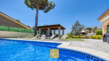 Piscina exterior privada en Villa Paris, con bordes de azulejos azules, múltiples tumbonas en el patio, una pérgola cubierta y una barbacoa de piedra al fondo.