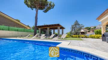 Piscina exterior privada en Villa Paris, con bordes de azulejos azules, múltiples tumbonas en el patio, una pérgola cubierta y una barbacoa de piedra al fondo.