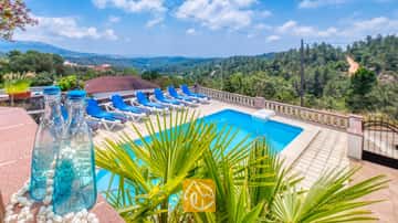 Piscina exterior privada en Villa Santa María con tumbonas azules en la terraza de baldosas y lejanas colinas verdes