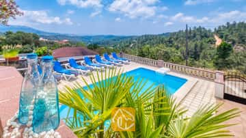 Piscina exterior privada en Villa Santa María con tumbonas azules en la terraza de baldosas y lejanas colinas verdes