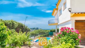 Vista exterior de Villa Valentina que muestra una piscina, tumbonas y arbustos de flores rosadas sobre una fachada blanca y amarilla.