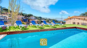 Piscina exterior de aguas azul turquesa en Villa Donna, equipada con cuatro tumbonas blancas y azules sobre césped artificial bajo un cielo despejado.