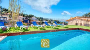 Piscina exterior de aguas azul turquesa en Villa Donna, equipada con cuatro tumbonas blancas y azules sobre césped artificial bajo un cielo despejado.