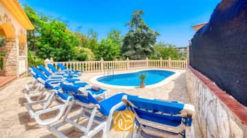 Piscina exterior privada en Villa Sarai rodeada de tumbonas azules, suelo de patio de piedra y árboles verdes bajo un cielo azul despejado