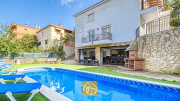 Piscina privada con tumbonas azules y patio de piedra en Villa Nicky, que cuenta con un exterior blanco de varios pisos, barbacoa al aire libre y zona de comedor en la terraza abierta.