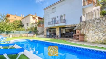 Piscina privada con tumbonas azules y patio de piedra en Villa Nicky, que cuenta con un exterior blanco de varios pisos, barbacoa al aire libre y zona de comedor en la terraza abierta.