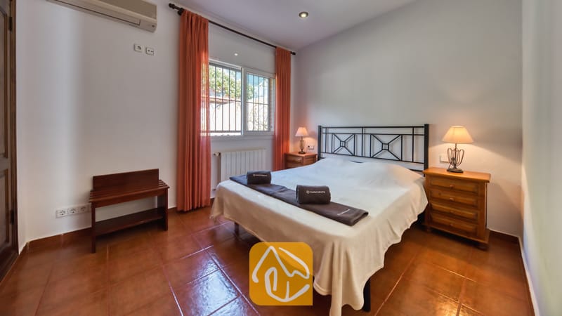 Dormitorio con cama doble, estructura de metal oscuro, cortinas naranjas que enmarcan la ventana y dos mesitas de noche de madera con lámparas.