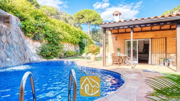 Piscina privada con una cascada de roca de piedra en Villa Alba, que muestra un patio exterior de ladrillo con muebles de comedor de madera y tejado de tejas.