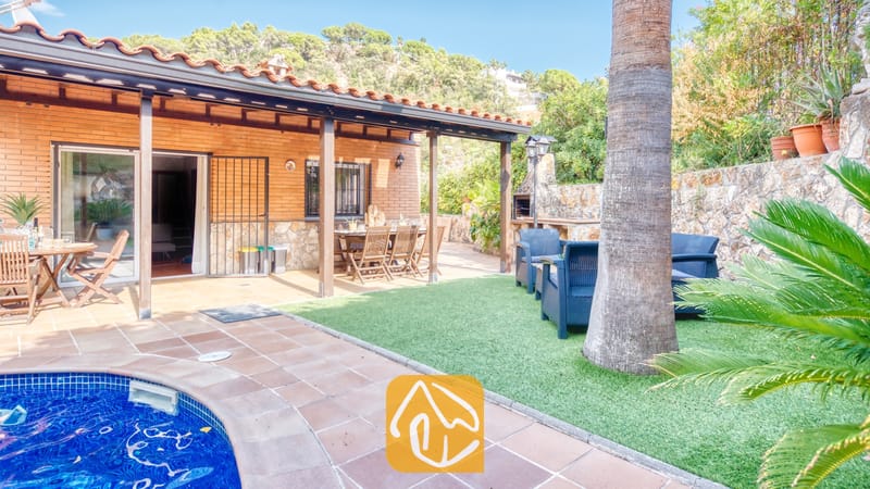 Terraza exterior y zona de piscina en Villa Alba, que cuenta con un patio cubierto con vigas de madera, mobiliario de comedor al aire libre y un césped delimitado por un muro de piedra