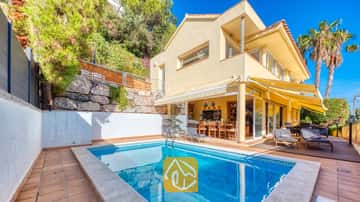 Piscina privada en Villa Santa Cristina con terraza de azulejos, toldos amarillos y tumbonas sobre una plataforma de madera junto a la fachada amarilla.