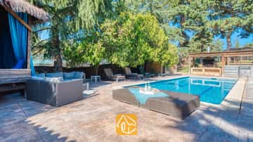 Piscina exterior privada en Villa Can Bernardi que cuenta con un sofá de ratán gris, tumbonas y una zona de barbacoa al aire libre rodeada de árboles.