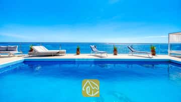 Piscina de vibrante azul en Villa Infinity, equipada con tumbonas blancas y macetas en la terraza de baldosas junto a la piscina, con vistas al mar