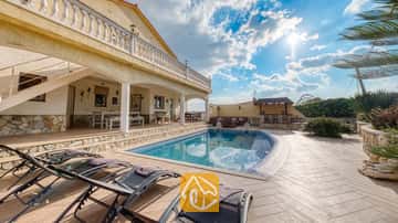 Piscina privada con tumbonas en la terraza pavimentada de Villa Madonna en España, que cuenta con un patio cubierto y paredes de piedra bajo un cielo soleado