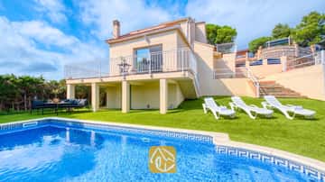 Exterior de Villa La Luna que muestra una piscina privada, tumbonas blancas sobre césped artificial y una casa beige de dos plantas con balcón bajo un cielo parcialmente nublado.