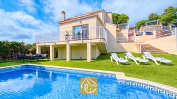 Exterior de Villa La Luna que muestra una piscina privada, tumbonas blancas sobre césped artificial y una casa beige de dos plantas con balcón bajo un cielo parcialmente nublado.