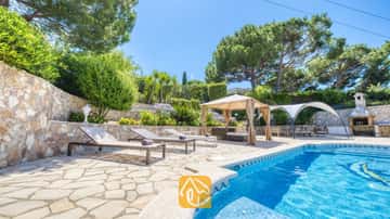 Piscina privada con tumbonas y patio de piedra en Villa Lorena, rodeada de pinos, jardines en bancales y un cenador con sombra.