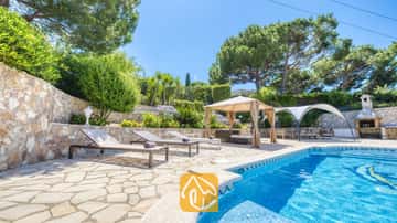 Piscina privada con tumbonas y patio de piedra en Villa Lorena, rodeada de pinos, jardines en bancales y un cenador con sombra.
