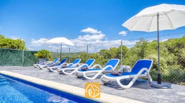 Tumbonas blancas y azules alineadas junto a la piscina de Villa Fransisca, acompañadas de sombrillas blancas bajo un cielo azul.
