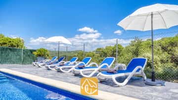 Tumbonas blancas y azules alineadas junto a la piscina de Villa Fransisca, acompañadas de sombrillas blancas bajo un cielo azul.