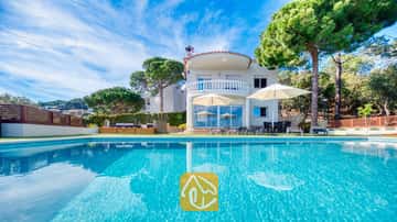 El exterior de Villa Chanel destaca por su piscina de aguas turquesas, sombrillas blancas en la terraza y un balcón de piedra de diseño curvo, todo ello rodeado de un frondoso entorno de pinos.