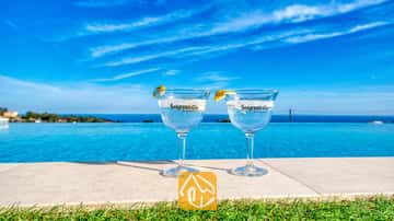 Dos cócteles de ginebra con rodajas de limón al borde de la piscina infinita de Villa Chanel, con vistas al azul del mar y el cielo.