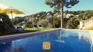 Piscina privada con borde de azulejos azules en Villa Noa, que cuenta con tumbonas sobre el césped y vistas a la colina bajo un cielo despejado.