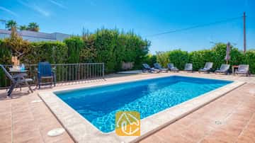 Piscina privada de aguas azuladas y tumbonas en la terraza pavimentada de Villa Yara, en España.