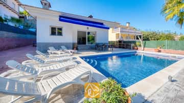 Piscina privada con tumbonas blancas alrededor de la terraza pavimentada de Villa Zarita bajo un cielo azul brillante.