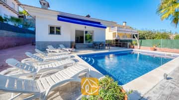 Piscina privada con tumbonas blancas alrededor de la terraza pavimentada de Villa Zarita bajo un cielo azul brillante.