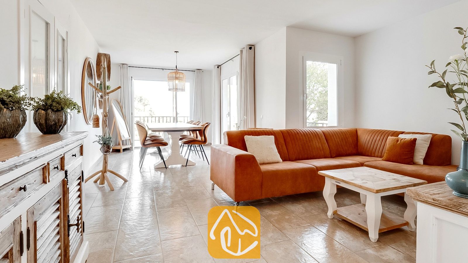 Luminosa sala de estar en Villa Tropicana que cuenta con un amplio sofá modular en tono marrón óxido, mesa de centro de madera y suelos de baldosas que conducen a un espacio de comedor.