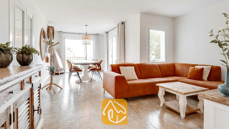 Luminosa sala de estar en Villa Tropicana que cuenta con un amplio sofá modular en tono marrón óxido, mesa de centro de madera y suelos de baldosas que conducen a un espacio de comedor.