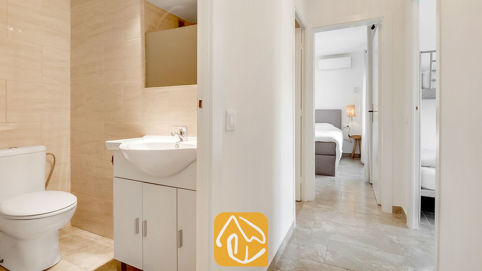 Baño con inodoro y lavabo de diseño blanco, que conecta con un pasillo con vistas a dos dormitorios.