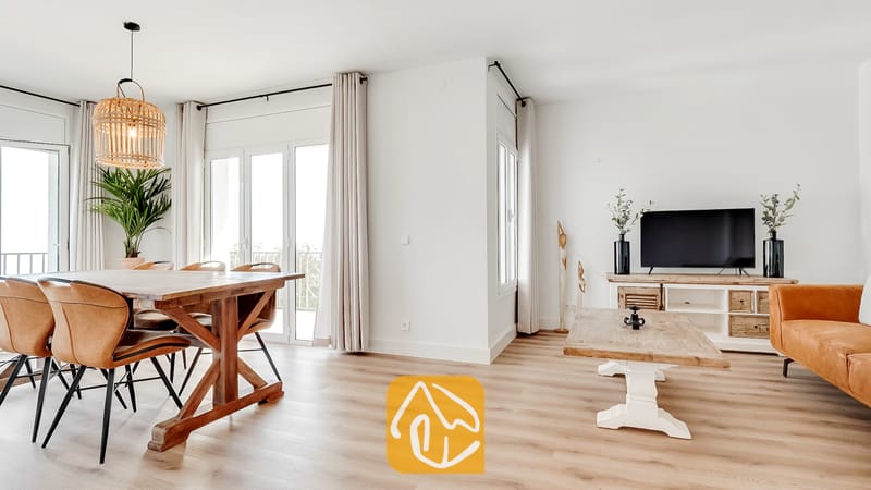 Amplia zona de estar y comedor en Villa Tropicana que cuenta con una mesa de comedor de madera, sillas de cuero marrón claro, suelos de madera clara y grandes puertas de cristal con cortinas en tonos neutros.