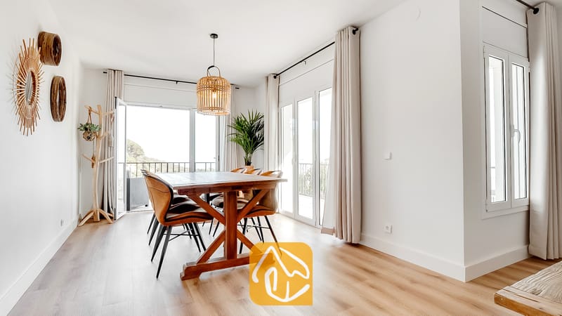 Comedor interior de Villa Tropicana que cuenta con una mesa de madera, sillas marrones e iluminación colgante de mimbre bajo paredes blancas y puertas de cristal.