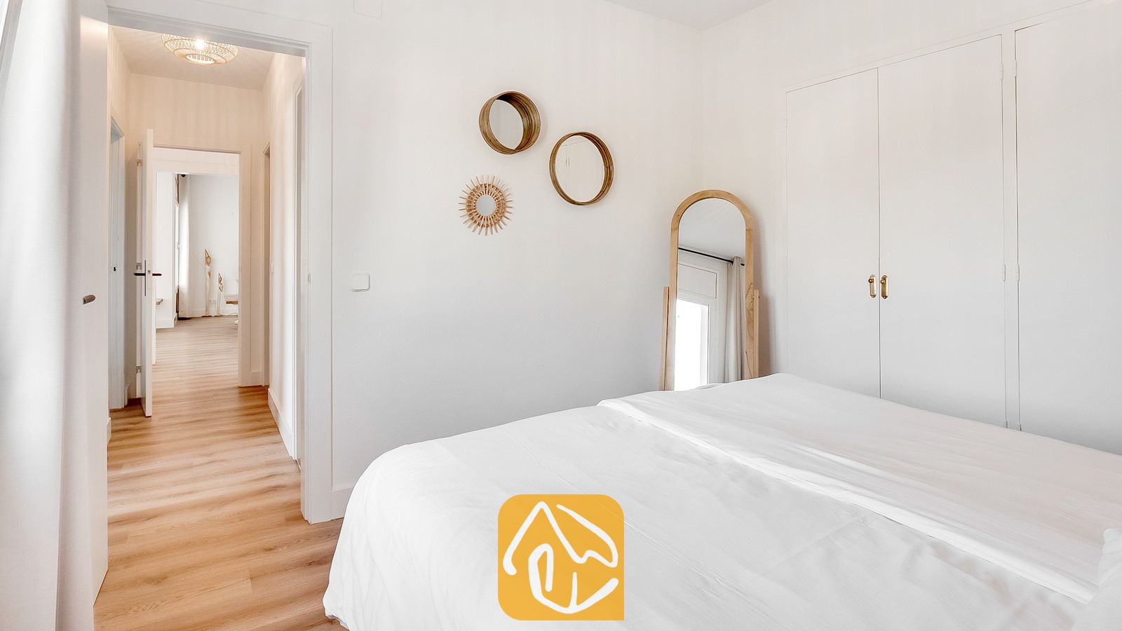 Dormitorio con cama blanca, suelos de madera, espejos de pared redondos y un espejo arqueado de cuerpo entero.