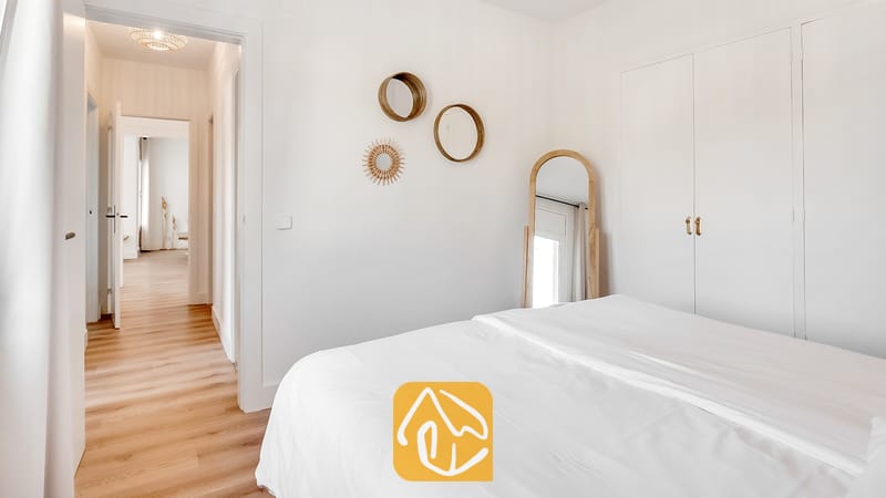 Dormitorio con cama blanca, suelos de madera, espejos de pared redondos y un espejo arqueado de cuerpo entero.