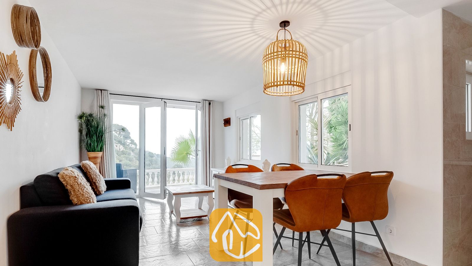 Salón y comedor de Villa Tropicana con una mesa de comedor de madera, sillas de cuero marrón y un sofá oscuro frente a unas puertas de cristal que se abren a un balcón.