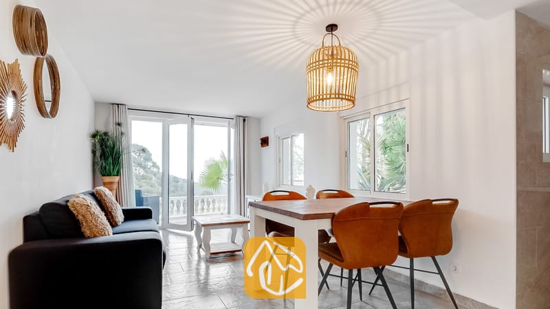 Salón y comedor de Villa Tropicana con una mesa de comedor de madera, sillas de cuero marrón y un sofá oscuro frente a unas puertas de cristal que se abren a un balcón.