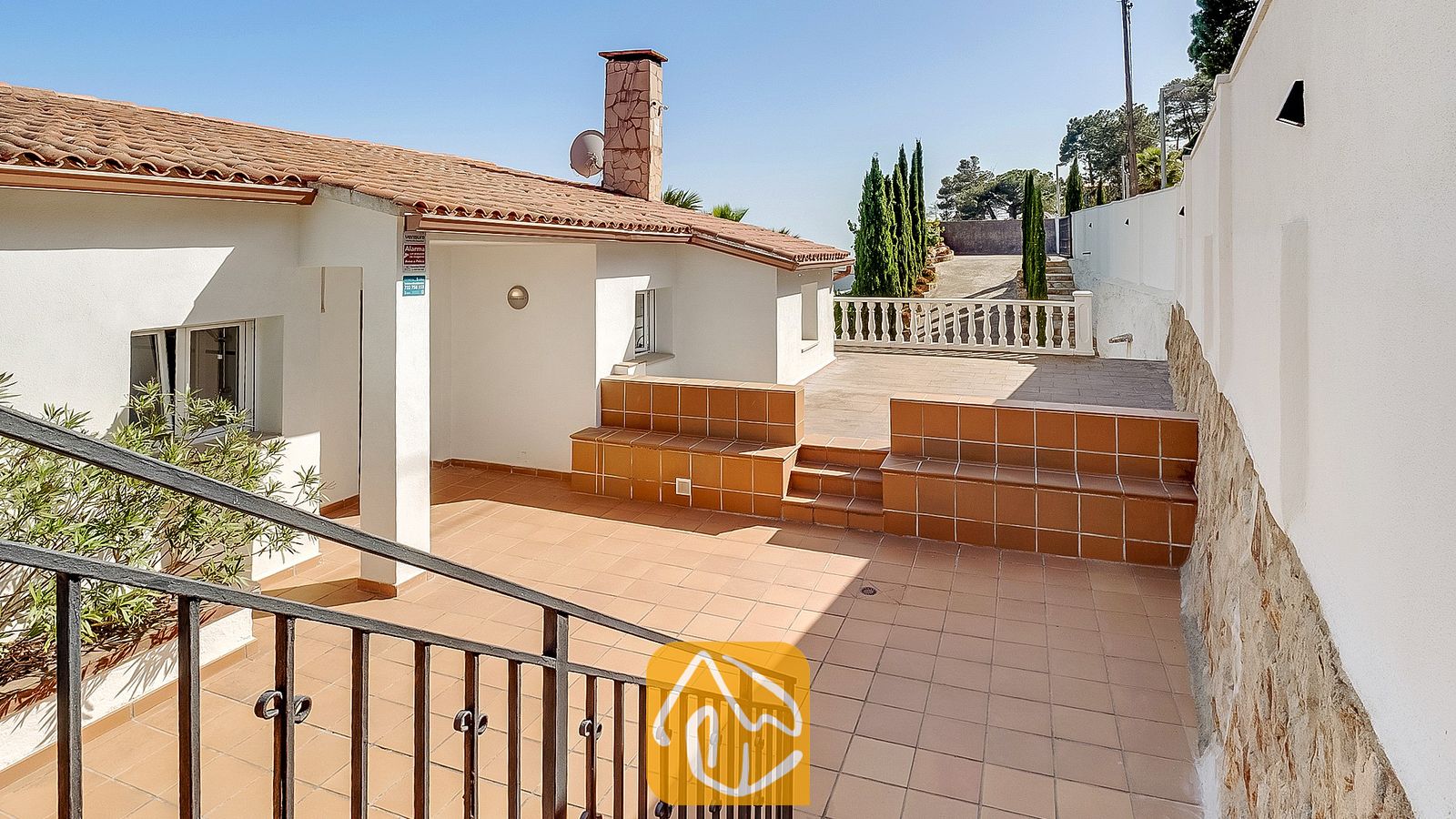 Terraza exterior de Villa Tropicana con suelo de baldosas, bancos de cerámica empotrados y una chimenea de piedra bajo un cielo azul despejado