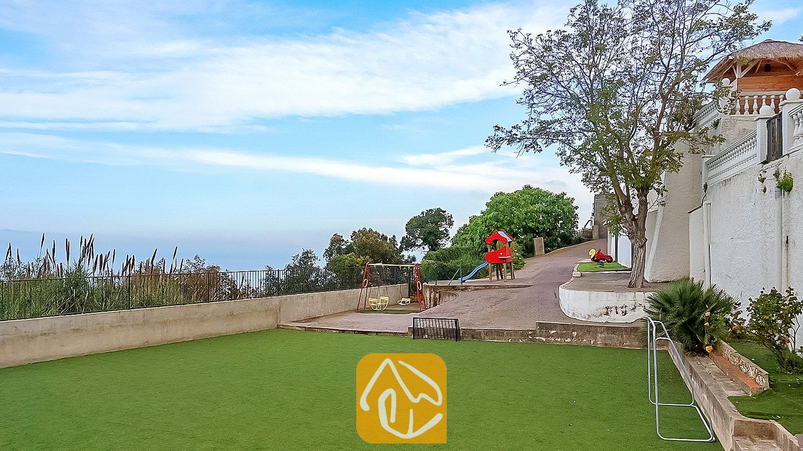 Área de juegos al aire libre en Villa Tropicana que cuenta con un columpio rojo, un tobogán y un césped artificial verde junto a una pared exterior blanca.