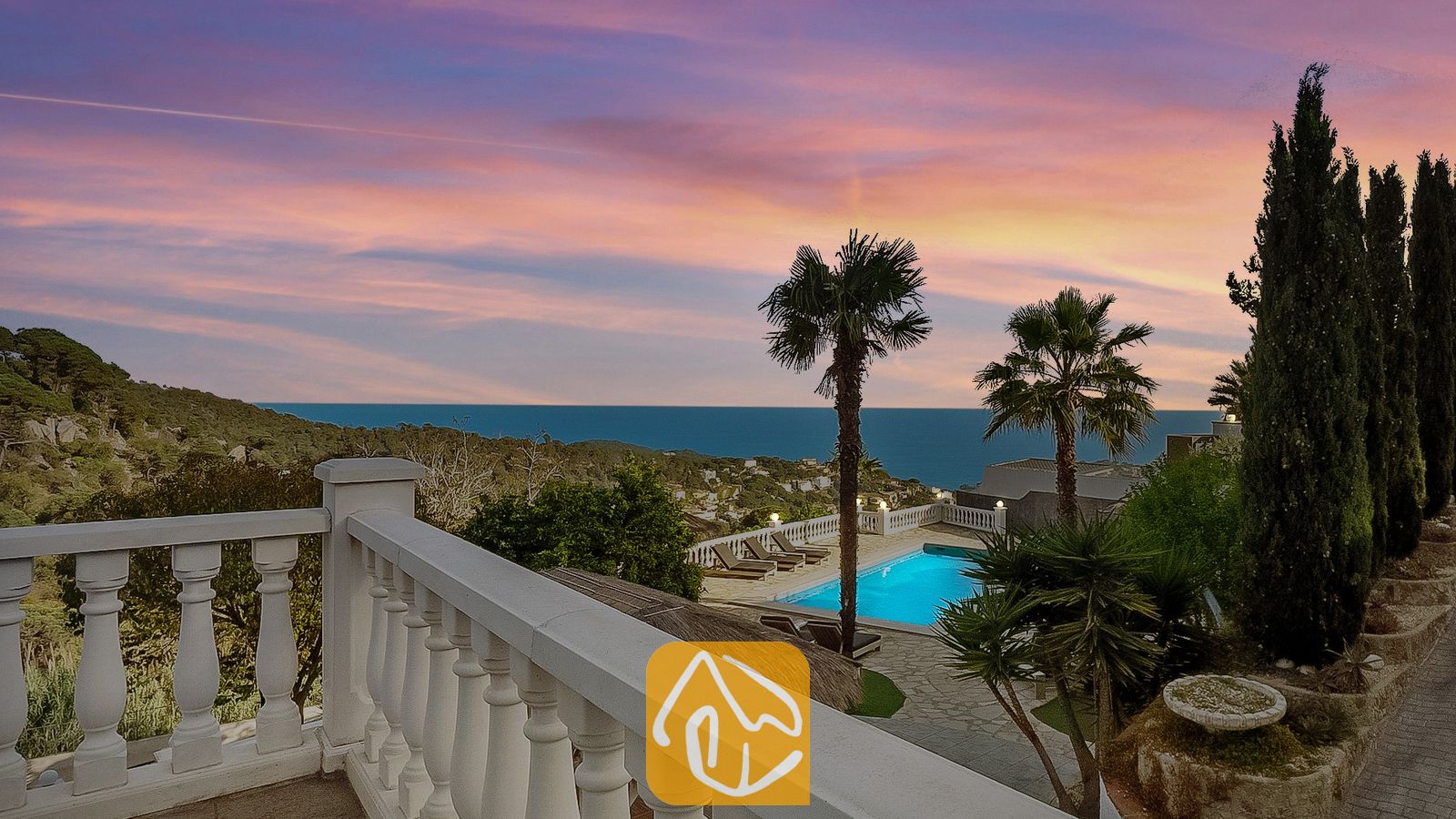 Terraza con vistas a Villa Tropicana, piscina privada, palmeras y vistas al mar bajo un cielo rosado y azul alAtardecer.