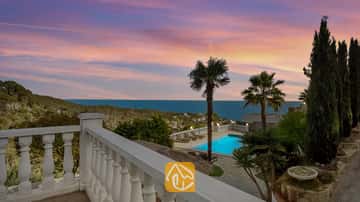 Terraza con vistas a Villa Tropicana, piscina privada, palmeras y vistas al mar bajo un cielo rosado y azul alAtardecer.