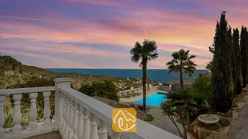 Terraza con vistas a Villa Tropicana, piscina privada, palmeras y vistas al mar bajo un cielo rosado y azul alAtardecer.