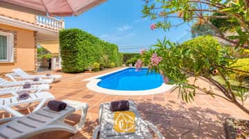 Piscina exterior privada en Villa Primavera rodeada de una terraza embaldosada, tumbonas blancas con toallas oscuras enrolladas y ramas de adelfas en plena floración.