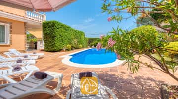 Piscina exterior privada en Villa Primavera rodeada de una terraza embaldosada, tumbonas blancas con toallas oscuras enrolladas y ramas de adelfas en plena floración.
