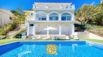 Exterior de Villa Sunrise que muestra una piscina rectangular de azulejos azules, tumbonas blancas y una villa amarilla de varias plantas con puertas de cristal arqueadas bajo un cielo despejado.